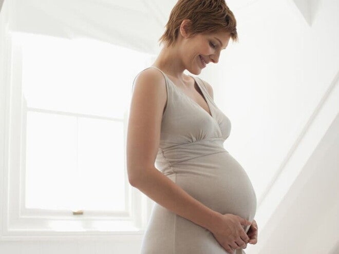 Femme enceinte tenant tendrement son ventre, illustrant l’importance de l’acide folique et des vitamines pendant la grossesse